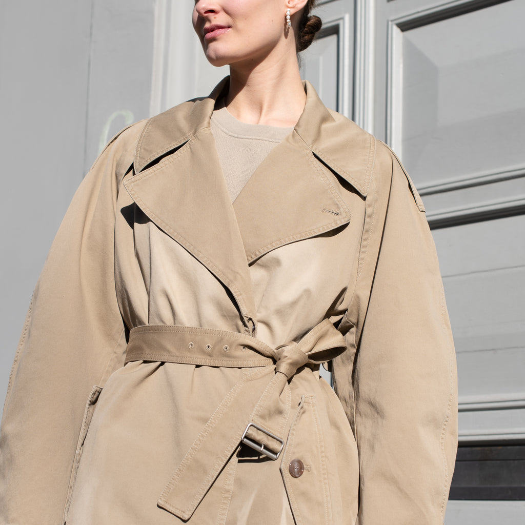 The Belted Trench Coat by Acne Studios is a cotton twill trench with a garment-dyed finish and an Acne Studios logo patch at the centre back