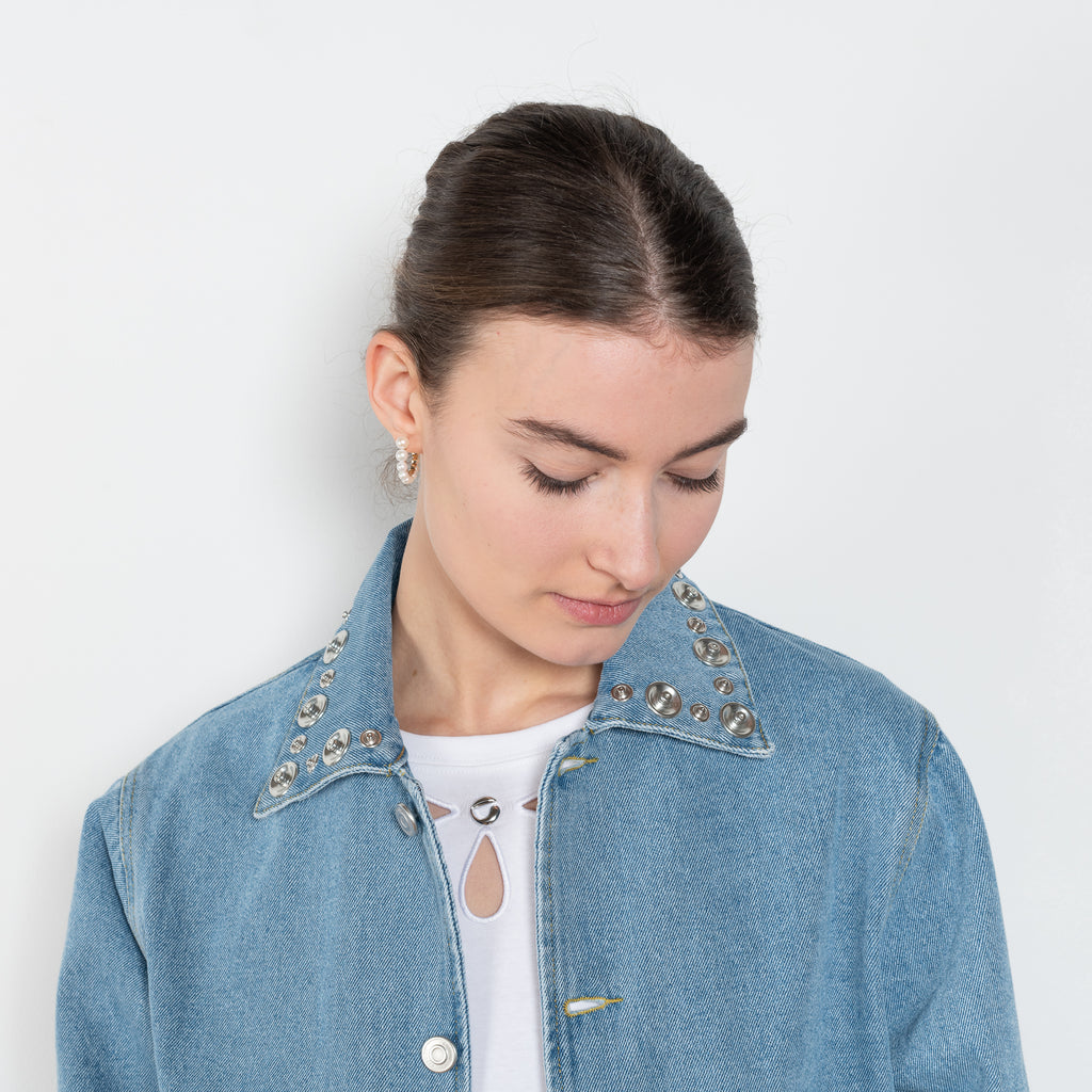 The Studded Denim Jacket by Coperni is a loose denim jacket with studded details and a front button closure